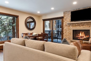 Living area with beige sofa, stone fireplace beneath a mounted TV, and a wooden dining table near sliding glass doors.