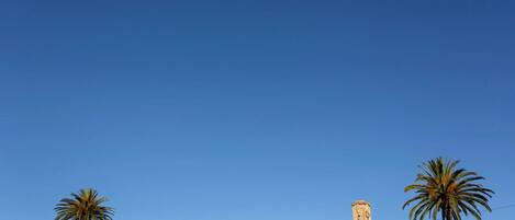 A tower on a grassy hill with palm trees, clear sky, and a few people in the distance.