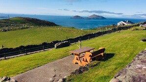 A coastal landscape with a grassy area, a wooden bench, and a stone wall. - Harbour View Snug Apartment | Spectacular Sea Views | Sleeps 2–4 (Caherdaniel)