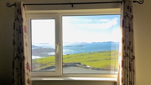 A window with a view of a green landscape and distant mountains. - Harbour View Snug Apartment | Spectacular Sea Views | Sleeps 2–4 (Caherdaniel)