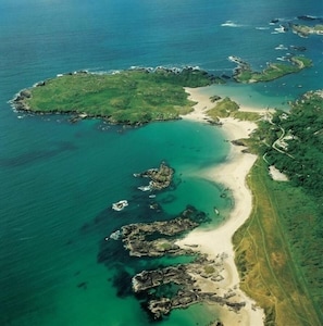 An aerial view of a coastal area with a sandy beach, rocky outcrops, and clear blue waters.