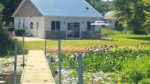 Een klein huis met een metalen dak, een steiger en een vijver met waterlelies.
