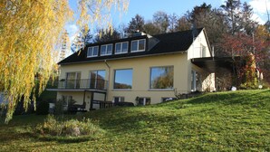 A two-story house with a balcony, a sloped roof, and a garden area. - OWL's Nest with a view over Detmold (Klüt)