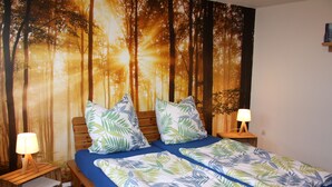 A bedroom with two beds, each with a blue mattress and leaf-patterned bedding. There are two bedside tables with lamps, and a wall mural of a forest scene. - OWL's Nest with a view over Detmold (Klüt)