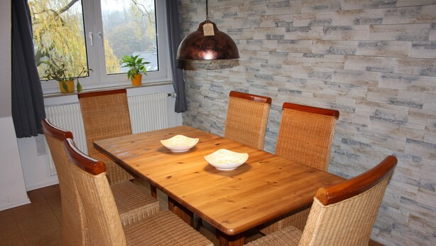 A dining area with a wooden table and wicker chairs, a hanging copper pendant light, and a brick-patterned wall. - OWL's Nest with a view over Detmold (Klüt)