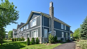 A two-story house with a stone chimney, large windows, and a well-maintained lawn.
