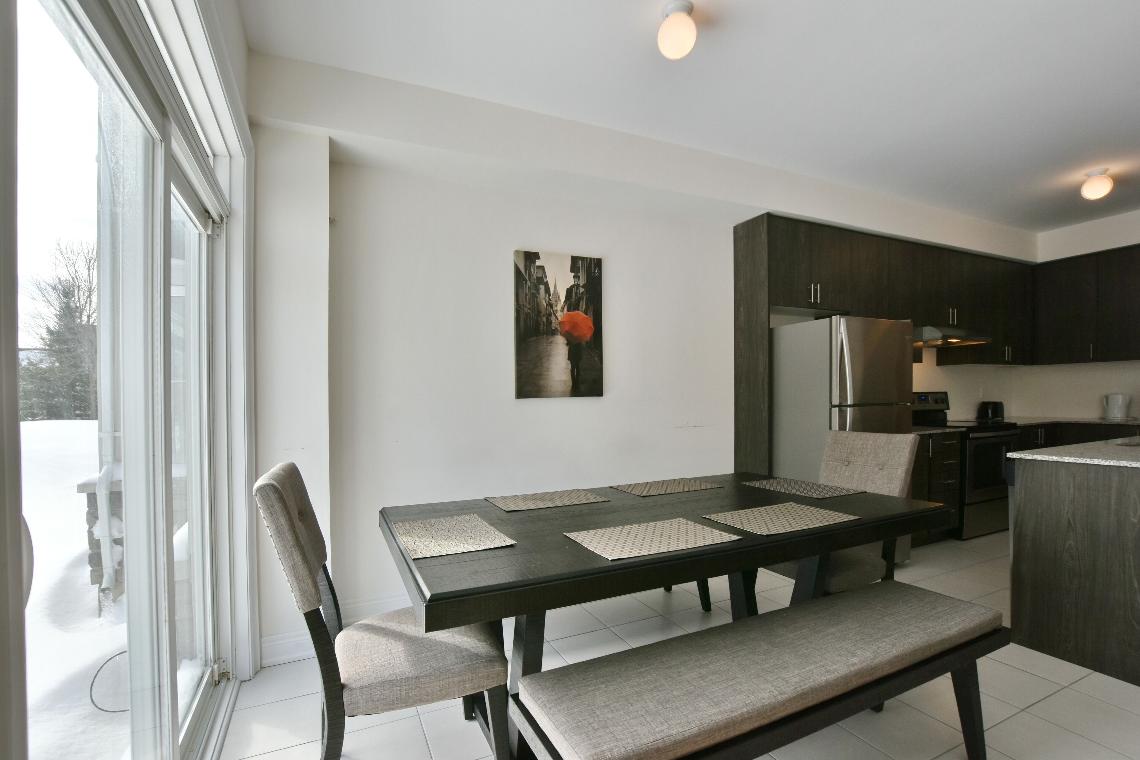 Una cocina moderna con armarios oscuros, un refrigerador de acero inoxidable y un comedor con mesa y sillas.