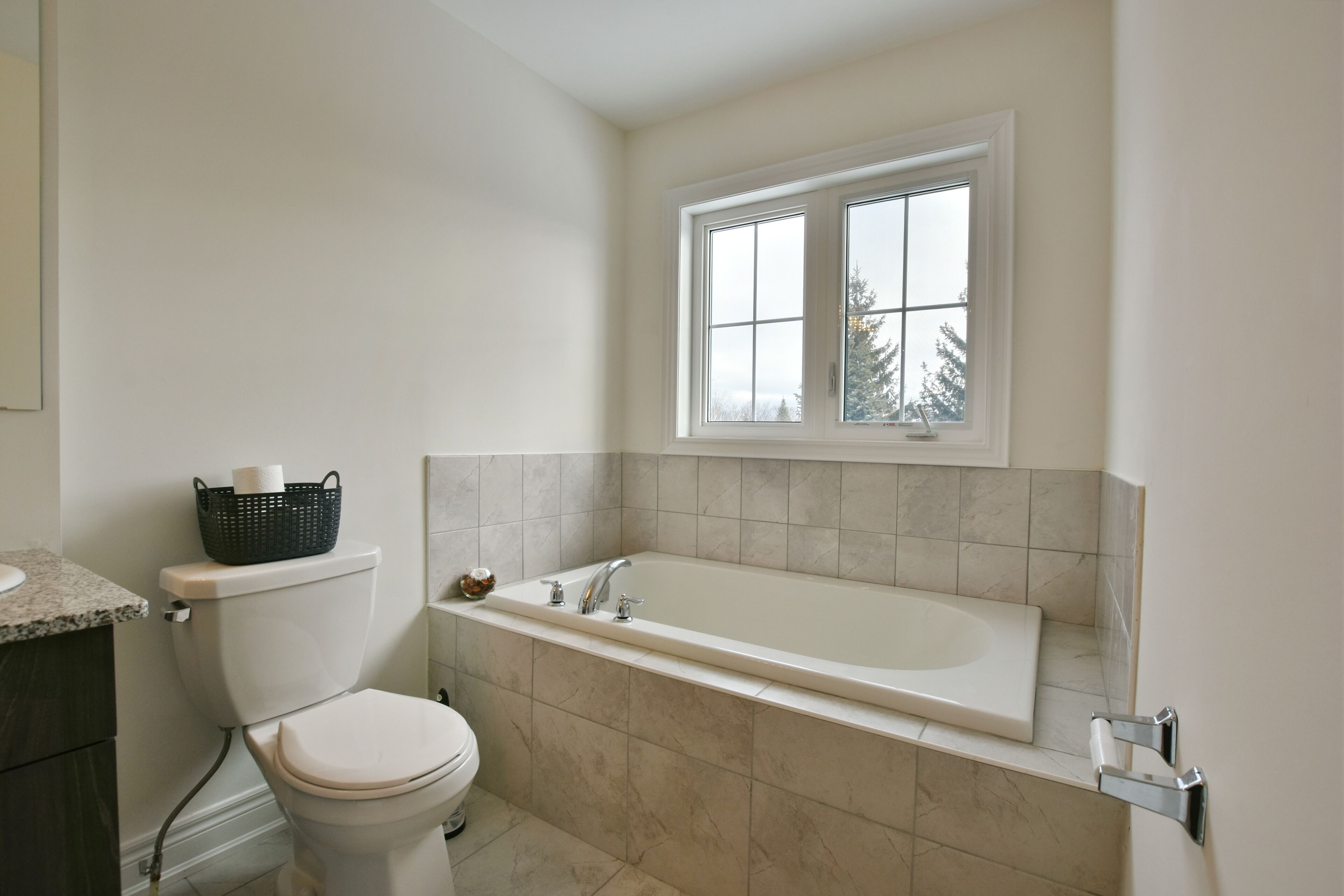 Une salle de bain avec des toilettes, une baignoire et une fenêtre située au-dessus de la baignoire.