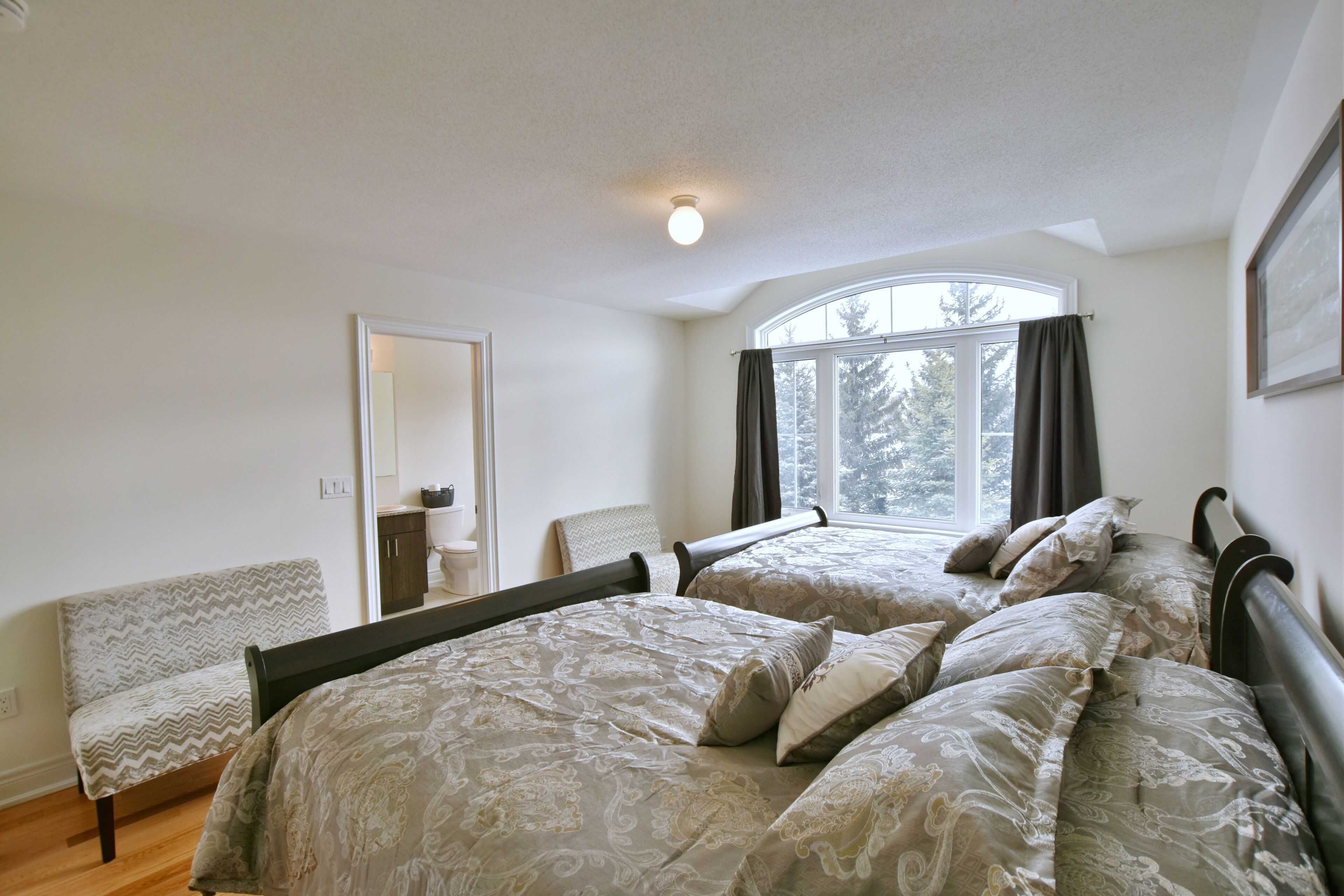 A bedroom with two beds, a bench, a window with curtains, and a door.