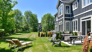 A backyard with a grill, chairs, and a lawn.