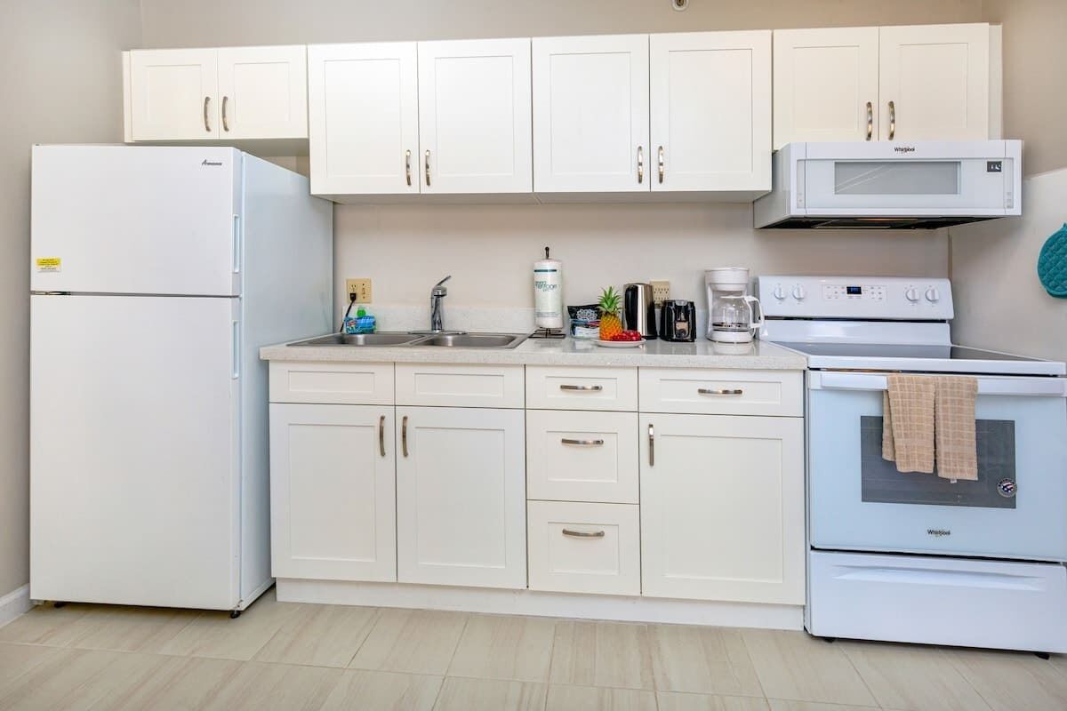 A kitchen with white cabinets, a refrigerator, a microwave, a coffee maker, and an oven.