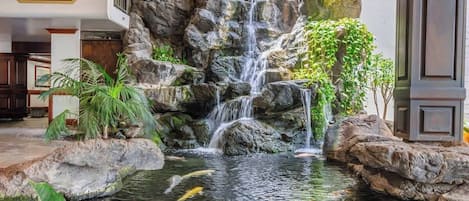 Ein Wasserfall mit Karpfen, umgeben von Steinen und Pflanzen, und ein Schild mit der Aufschrift 'Tower I Makai'.