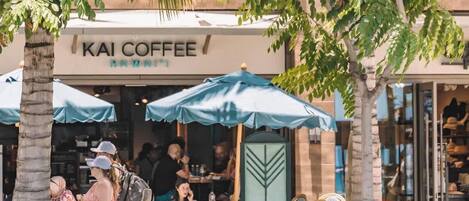 Una cafetería llamada 'KAI COFFEE' con terraza y palmeras.