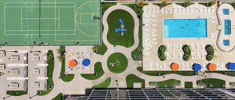 An aerial view of a hotel with a tennis court, swimming pool, and outdoor seating areas.