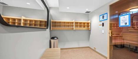 A modern bathroom with a wooden bench, built-in shelves, and a glass door leading to a seating area.