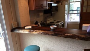 A kitchen with a wooden countertop, two stools, a stove, and cabinets.