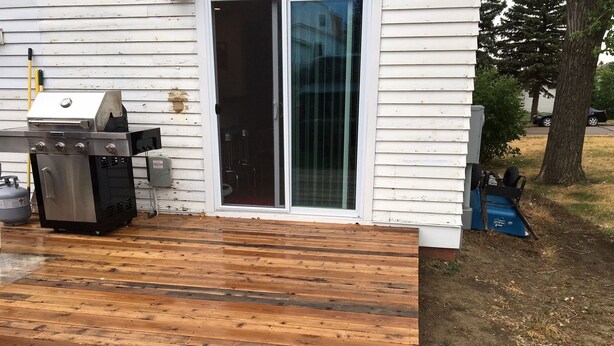 A wooden deck with a grill and a gas tank.