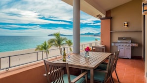 A balcony with a wooden table and chairs, overlooking a beach and ocean. - Beachfront Paradise, right on the ocean! (San José Del Cabo)