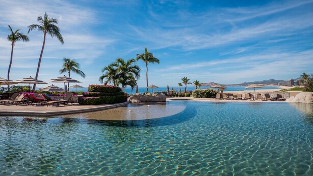 A clear pool with lounge chairs and umbrellas, surrounded by palm trees and a view of the ocean. - Beachfront Paradise, right on the ocean! (San José Del Cabo)