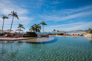 A clear pool with lounge chairs and umbrellas, surrounded by palm trees and a view of the ocean. - Beachfront Paradise, right on the ocean! (San José Del Cabo)
