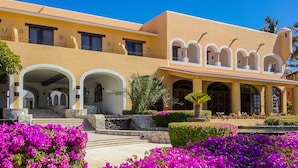 A two-story building with a yellow facade, multiple balconies, and a central courtyard with vibrant purple flowers. - Beachfront Paradise, right on the ocean! (San José Del Cabo)