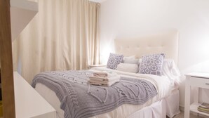 Een net opgemaakt bed met een wit hoofdeinde, een grijze gebreide deken en bedpillows met een patroon.