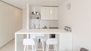 Een moderne keuken met een wit aanrecht, twee witte barstoelen, een koffiezetapparaat en een klok aan de muur.