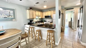 A kitchen with wooden cabinets, a central island with stools, a microwave, and a stove. - Perfect Location ~ Ocean Reef 601 ~ On the beach ~ Walk to Dining & Shopping (Gulf Shores)