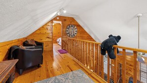 Une chambre mansardée chaleureuse avec un plafond en bois, un canapé en cuir noir, une rambarde en bois et un ours en peluche.