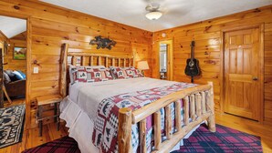 Une chambre dans un chalet en bois, avec un lit, une guitare et une décoration représentant un ours accrochée au mur.