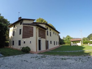 A two-story building with a beige facade, a wooden lattice window, and a small attached structure with a tiled roof. - CASALE LA FATA, FLORA delightful two bedroom pool front apartment (CAMAIORE)