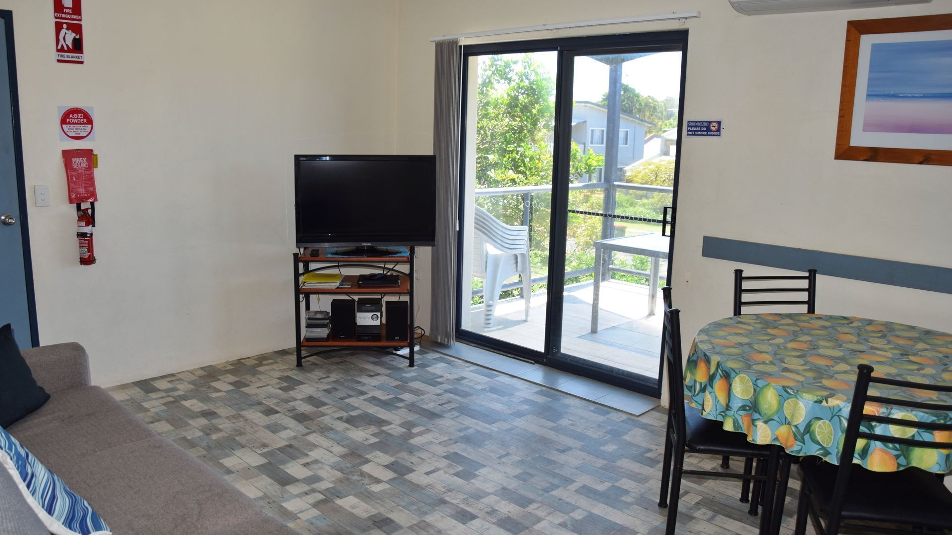 Une pièce équipée d’un téléviseur à écran plat posé sur un meuble, d’une table à manger avec des chaises, d’un canapé, d’un extincteur et d’une couverture anti-feu accrochée au mur.