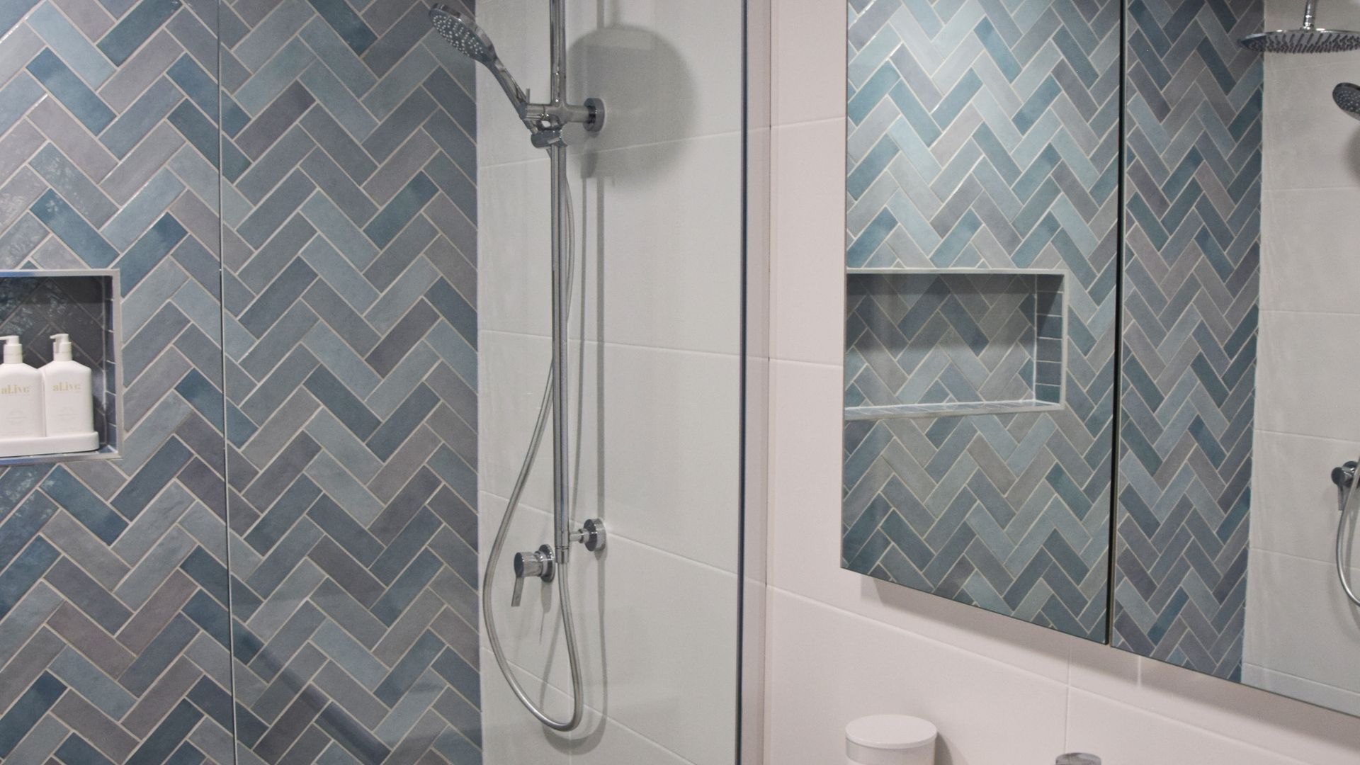 Une salle de bain avec un carrelage disposé en motif de chevron, une douche en verre et un miroir orné d’un motif de carrelage similaire.