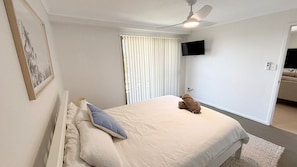 Un dormitorio con cama, ventilador de techo, televisor y ventana con persianas.