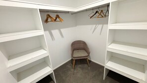 A corner closet with white shelves, a wicker chair, and wooden hangers. - Waterford Apartment 3 - Bring your own linen (South West Rocks)