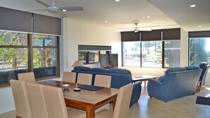 Uma sala de estar moderna com uma mesa de madeira, sofás azuis e grandes janelas com vista para o exterior.