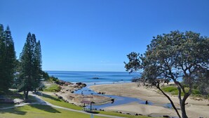 A coastal landscape with a clear view of the sea, a sandy beach, and a small pond with rocks. - Waterford Apartment 3 (South West Rocks)