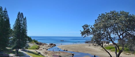 A coastal landscape with a clear view of the sea, a sandy beach, and a small pond with rocks.