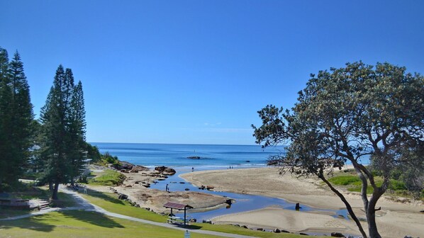 A coastal landscape with a clear view of the sea, a sandy beach, and a small pond with rocks.