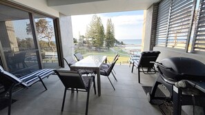 A balcony with a table and chairs, a grill, and a view of the ocean and trees. - Waterford Apartment 3 - Bring your own linen (South West Rocks)