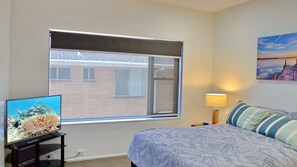 Enjoy a peaceful retreat with a view of the city from the large window, featuring a comfortable bed, a bedside lamp, and a TV displaying an underwater scene.
