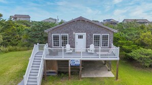 A two-story wooden house with a covered porch and a small staircase leading to the deck.