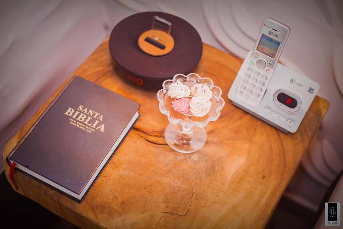 A book titled 'Santa Biblia', a rotary dial telephone, and a glass dessert on a wooden surface.