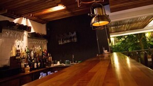 Eine Bar mit Holzbalkendecke, hängenden Lampen und einer Theke mit Flaschen und Gläsern.