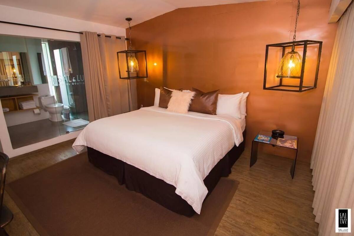 A modern hotel room with a large bed, two bedside tables, a mirror, and a view of the bathroom.