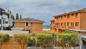 A coastal residential area with modern brick buildings, a fenced garden, and a view of the sea.