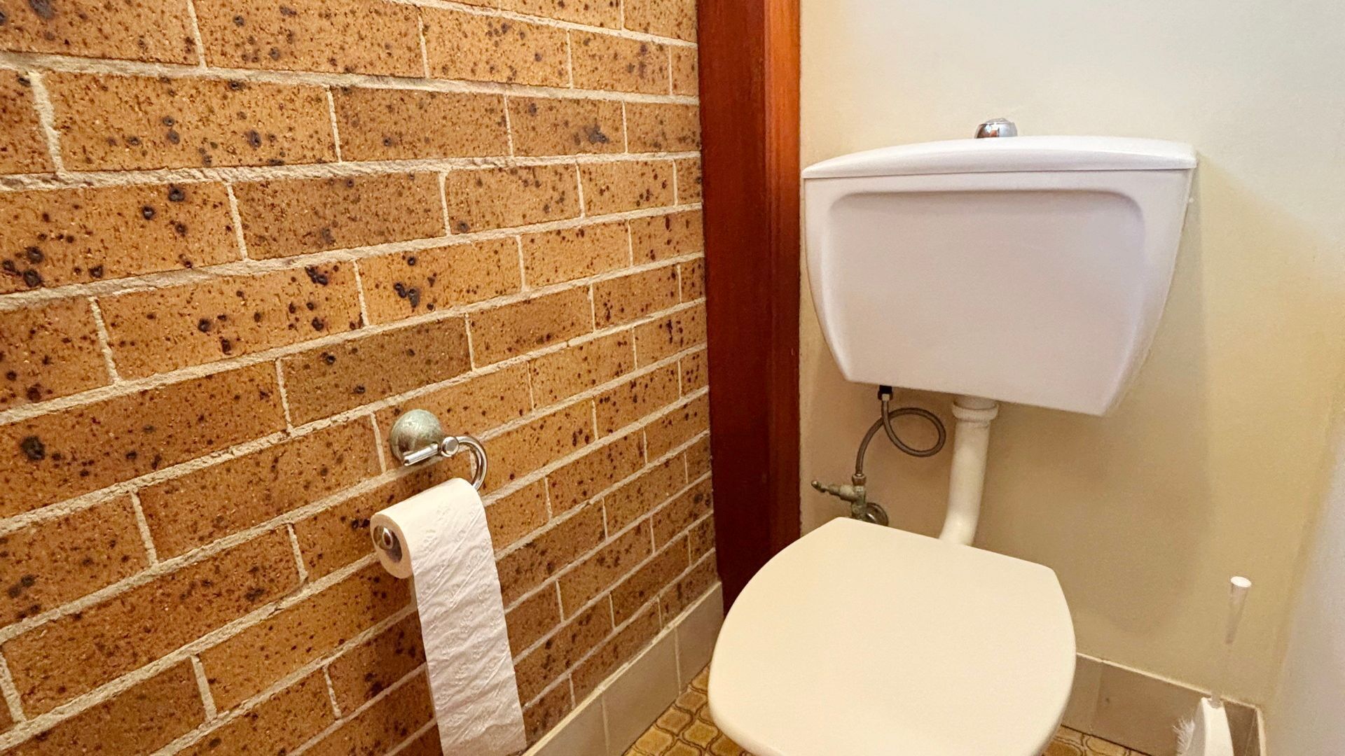 Une salle de bain avec des toilettes, un rouleau de papier toilette posé sur un support et un mur blanc orné d’un motif en briques.