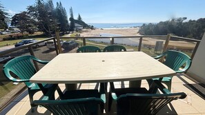 A balcony with a table and chairs, overlooking a beach and ocean. - Main Beach 1 - beachfront (South West Rocks)