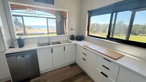 A modern kitchen with a dishwasher, a sink, and a window overlooking a grassy area. - Main Beach 1 - beachfront (South West Rocks)