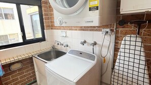 A compact laundry room with a washing machine, a dryer, and a wall-mounted ironing board. - Main Beach 1 - beachfront (South West Rocks)